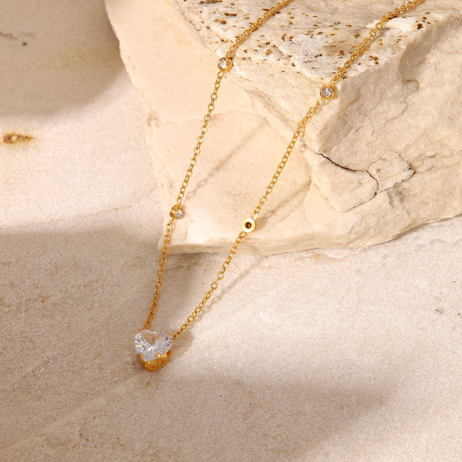 Gold necklace with a heart-shaped pendant on a beige stone surface