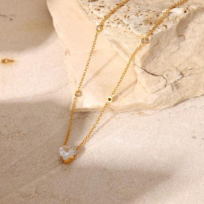 Gold necklace with a heart-shaped pendant on a beige stone surface