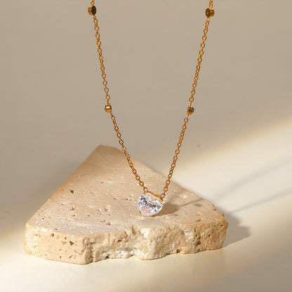 Gold necklace with a heart-shaped pendant on a stone surface