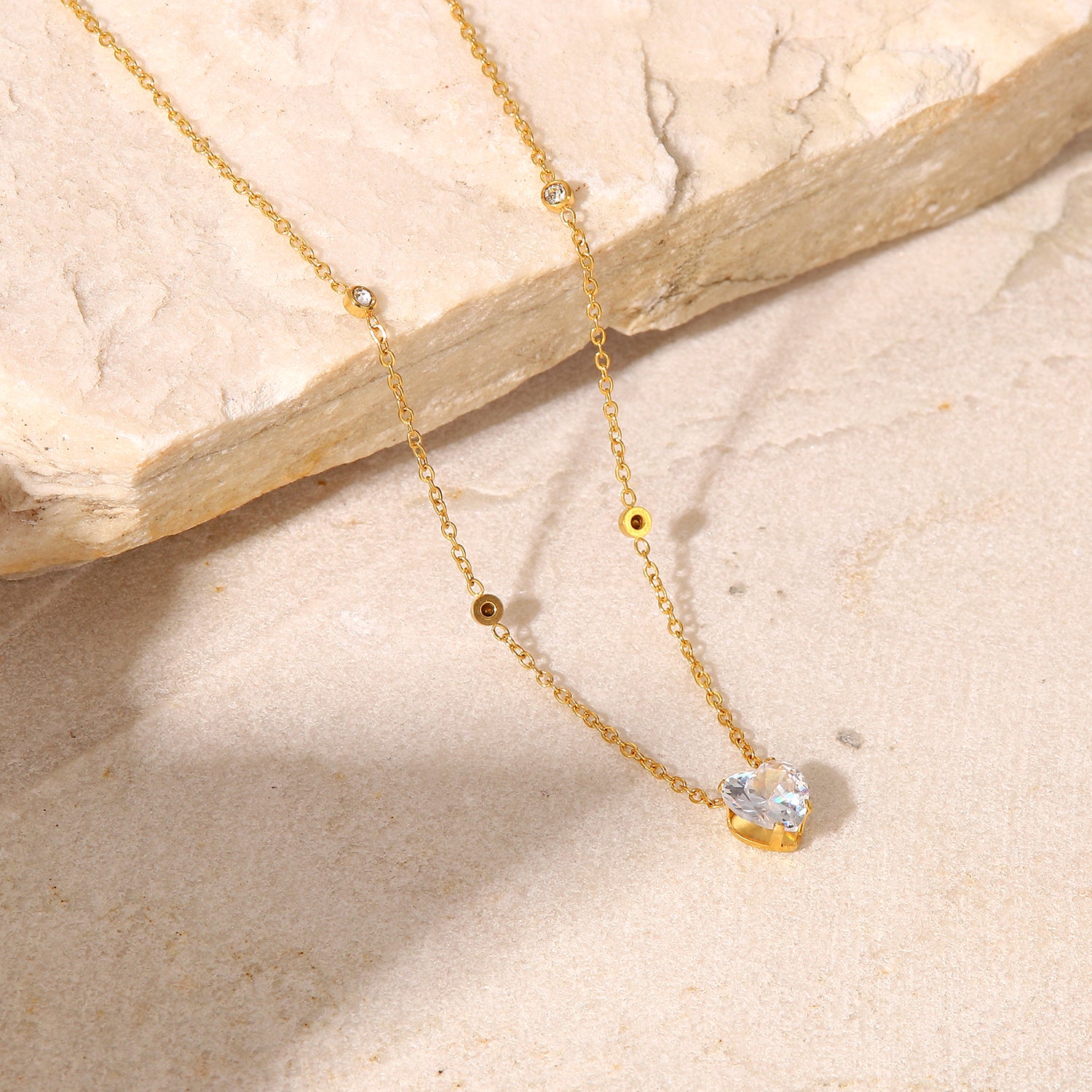 Gold necklace with a heart-shaped pendant on a beige stone surface