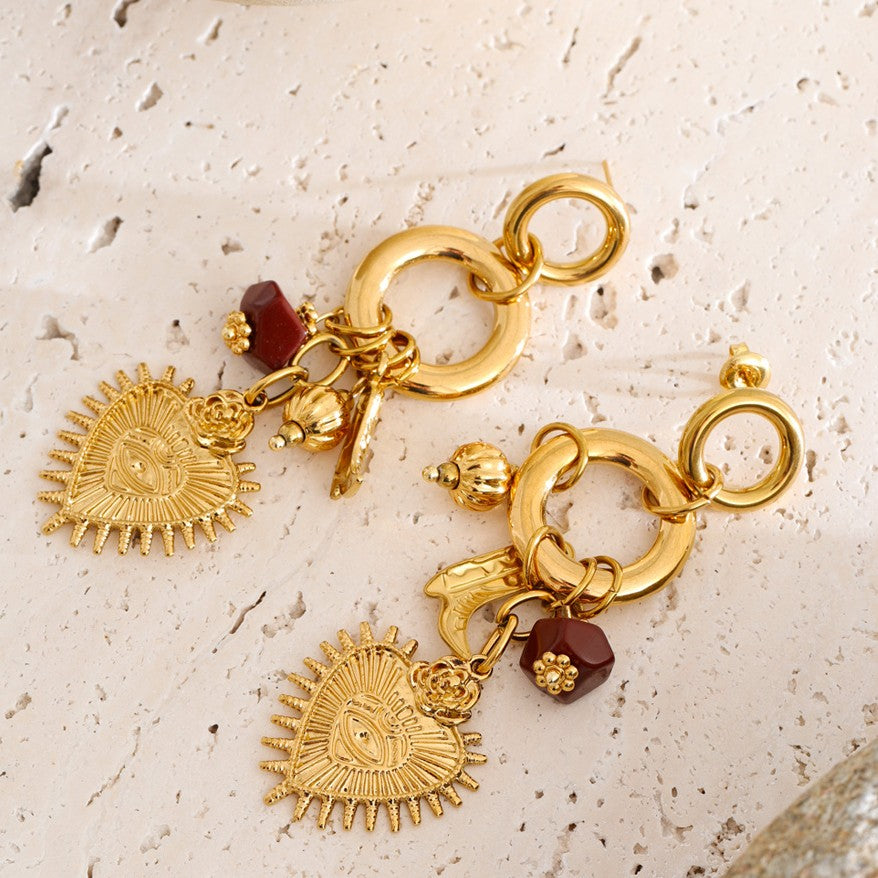 Gold charm earrings with sun designs on a textured beige surface