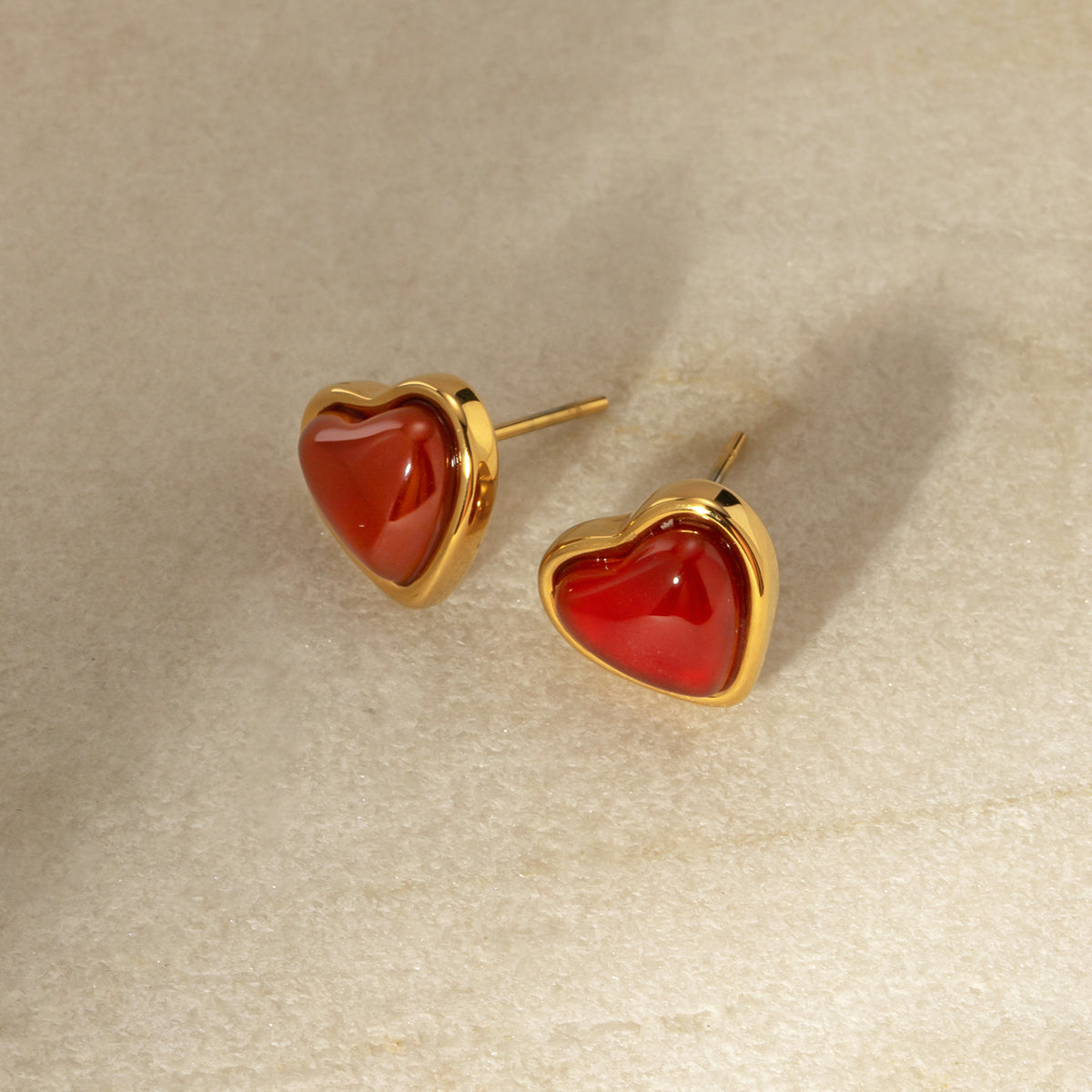 Elegant heart-shaped earrings with red stones and gold frames on a beige background