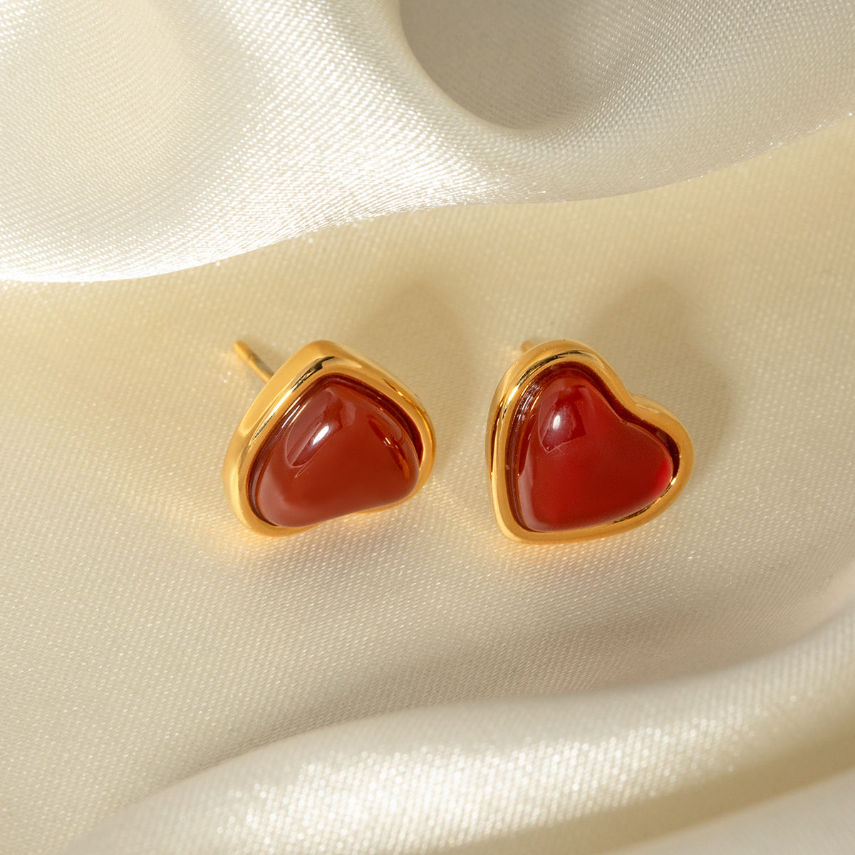 Elegant heart-shaped earrings with red stones and gold frames on a beige fabric background