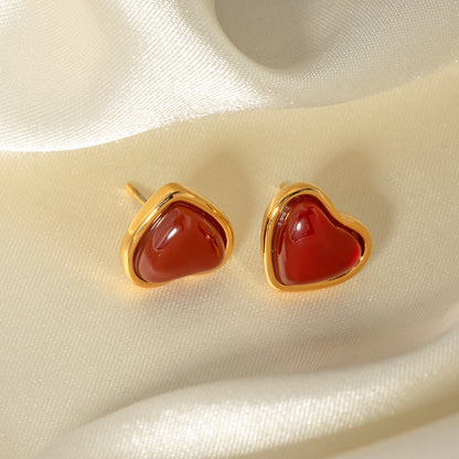 Elegant heart-shaped earrings with red stones and gold frames on a beige fabric background