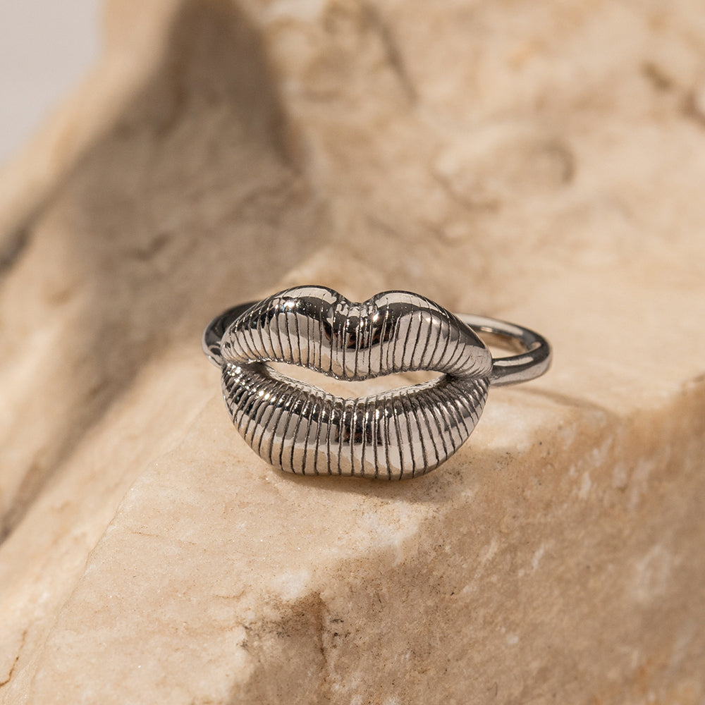 Silver ring shaped like lips on a textured beige surface