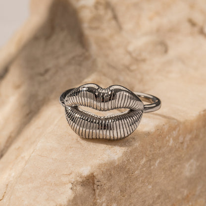 Silver ring shaped like lips on a textured beige surface