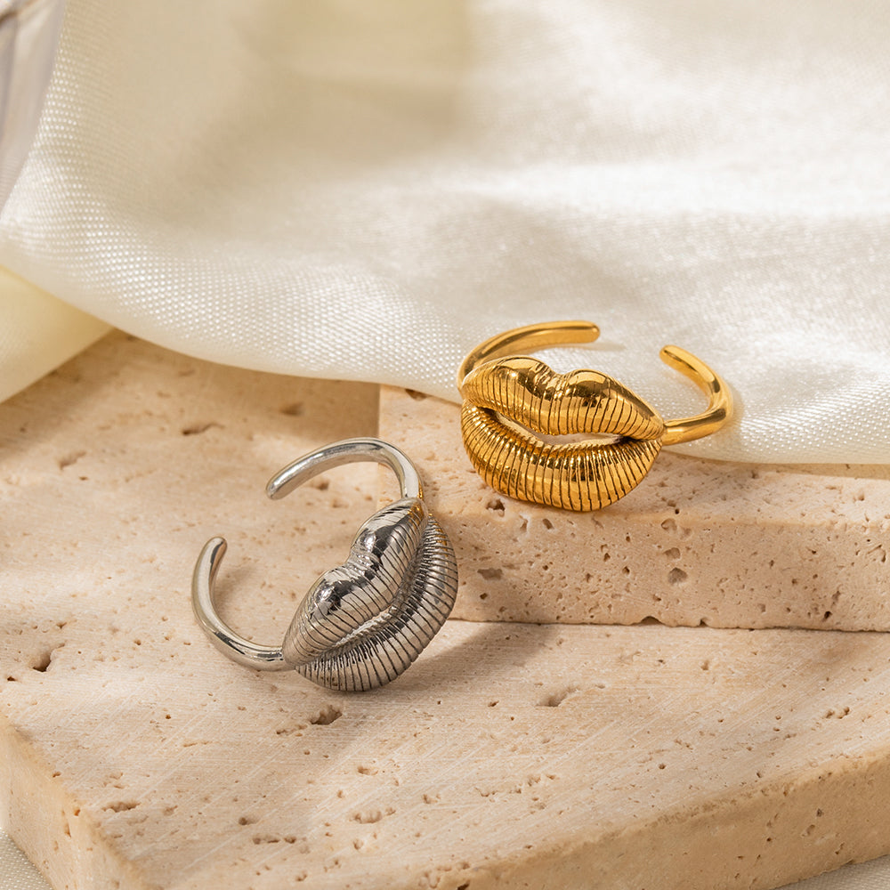 Gold and silver leaf-shaped rings on a beige stone surface with a white fabric background