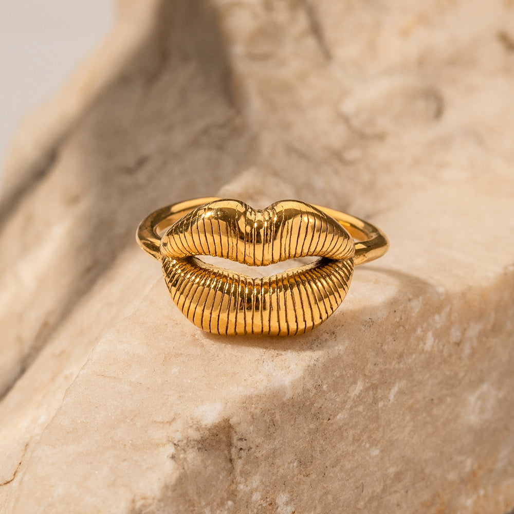 Gold lip-shaped ring on a textured beige surface