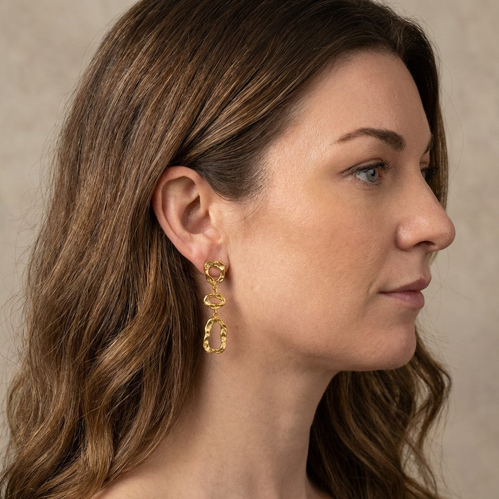 Close-up of a woman wearing gold stainless steel earrings against a neutral background