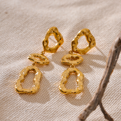 Long gold earrings on a textured beige surface with a branch