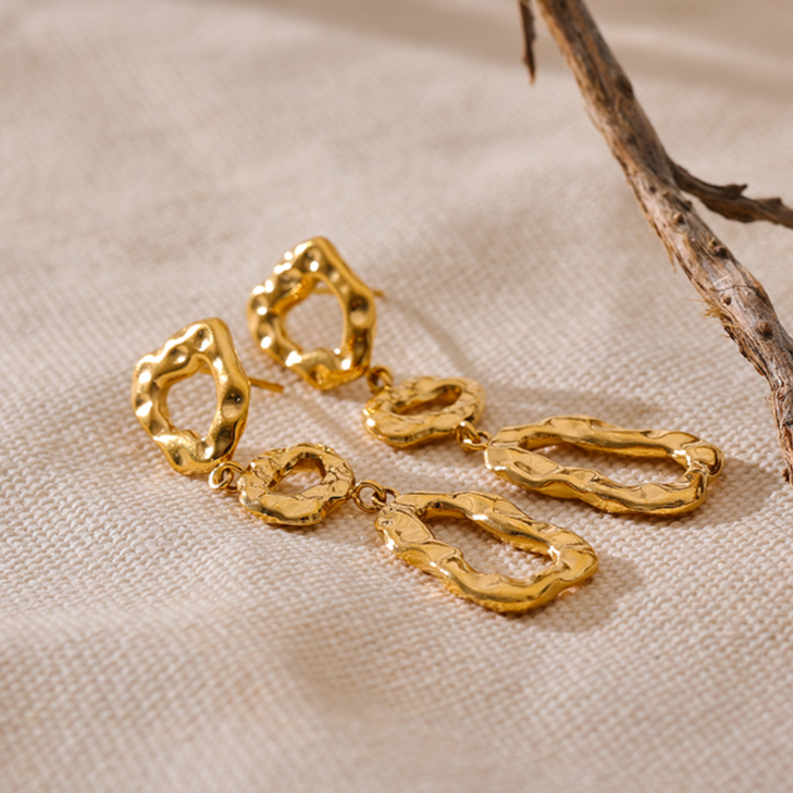 Gold earrings on a beige fabric background