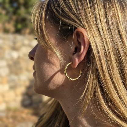 Close-up of a person wearing a gold hoop earring with a blurred natural background