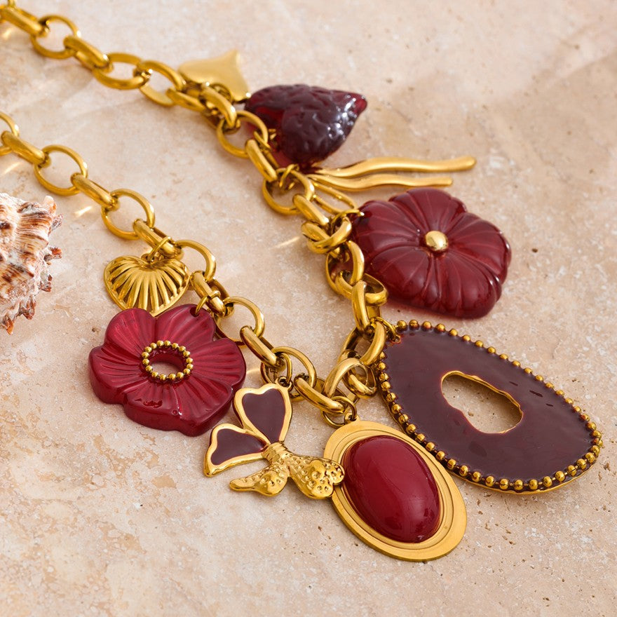 Gold stainless steel necklace with red and purple charms on a beige surface