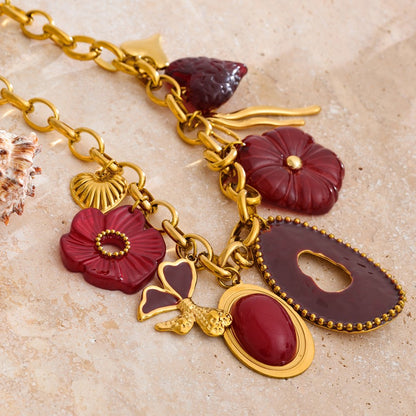 Gold stainless steel necklace with red and purple charms on a beige surface