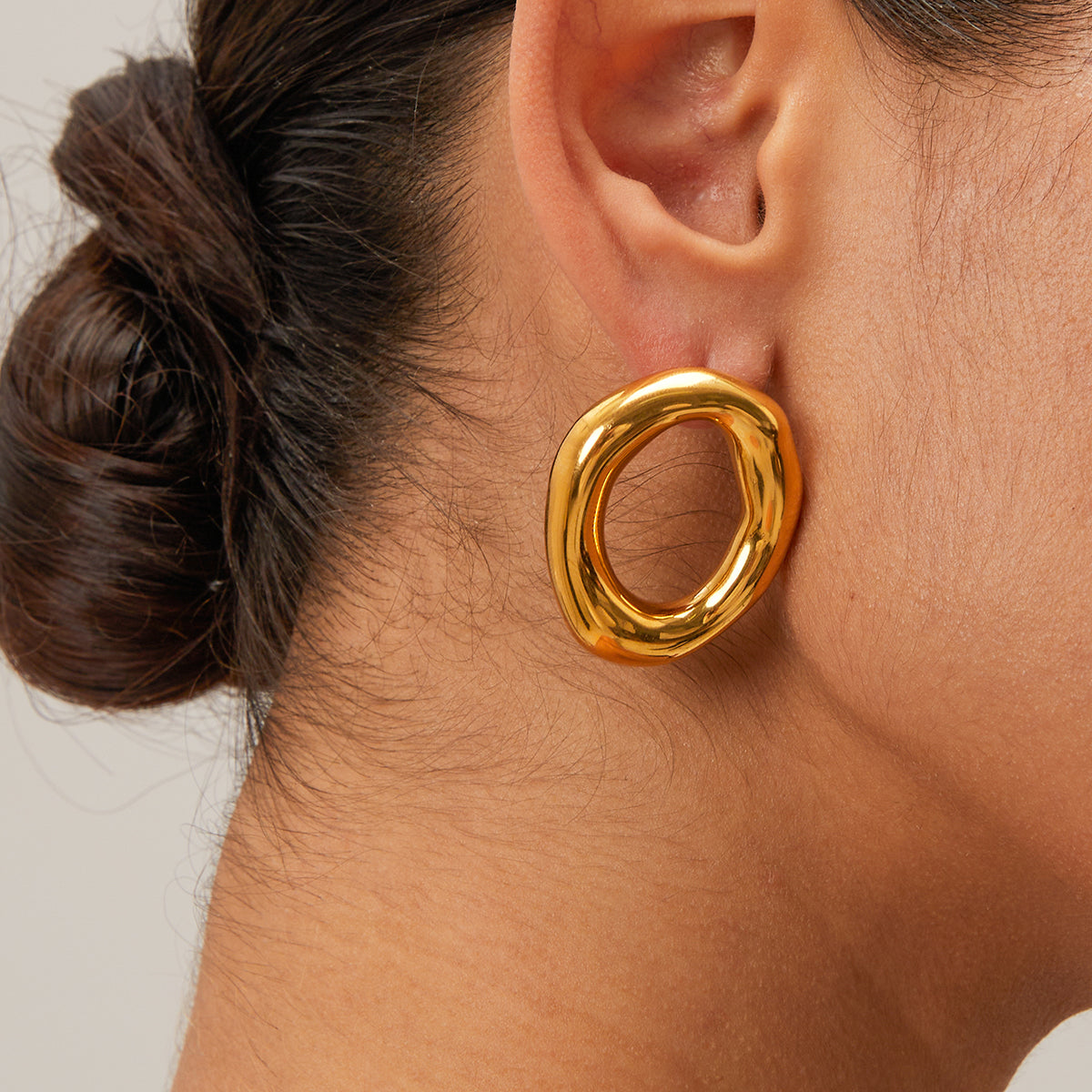 Gold waterproof earring worn by a person with a neutral background