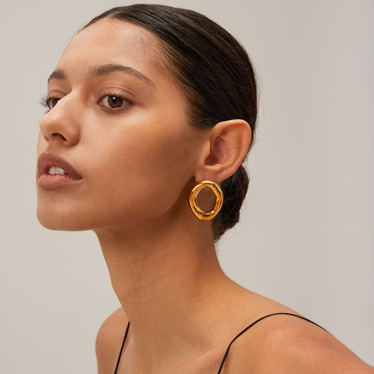 Woman wearing a gold chunky earring against a neutral background