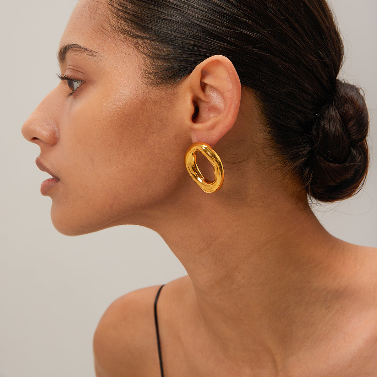 Woman wearing a gold statement earring against a neutral background