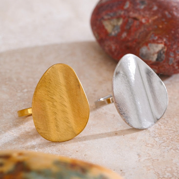 Gold and silver ring on a textured surface with a stone in the background