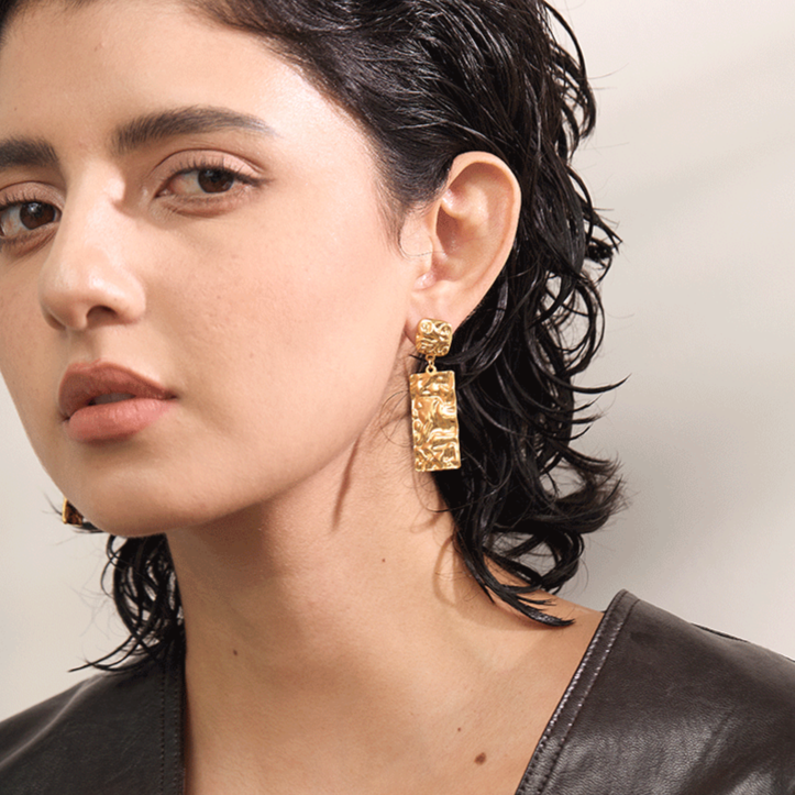 Close-up of a woman wearing gold waterproof earrings with a neutral background