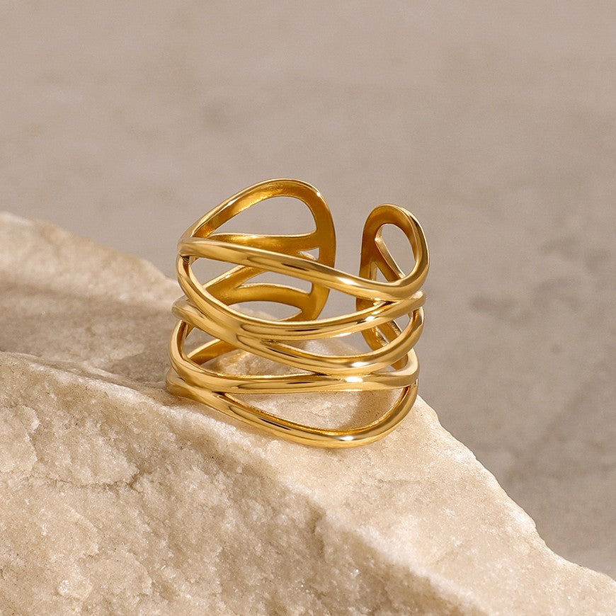 Gold ring with a wavy design on a beige stone surface