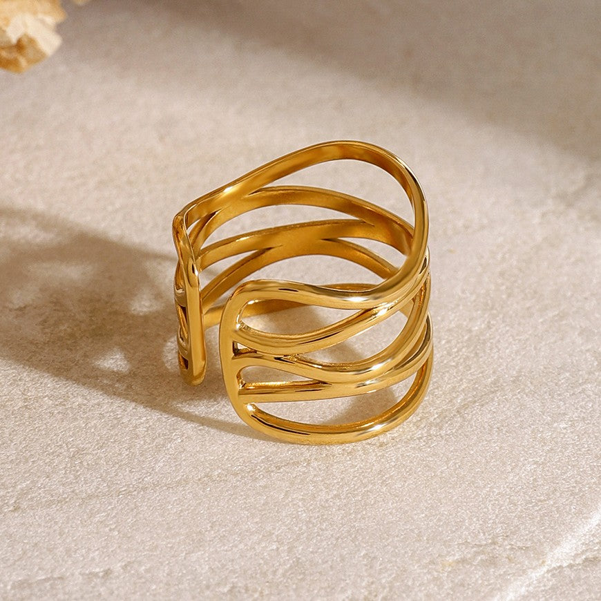 Gold ring with wavy design on a beige surface