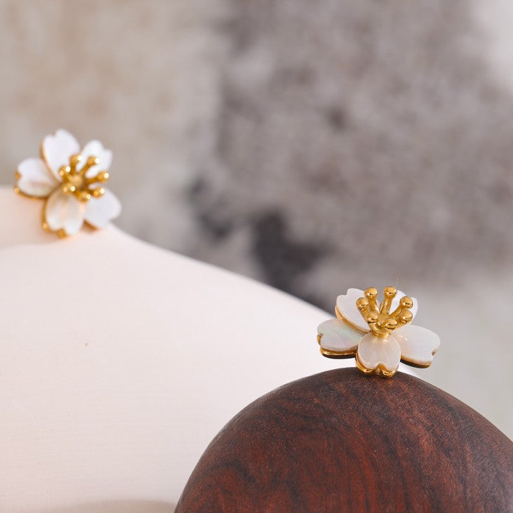 Gold and white floral earrings on a wooden surface with a blurred background