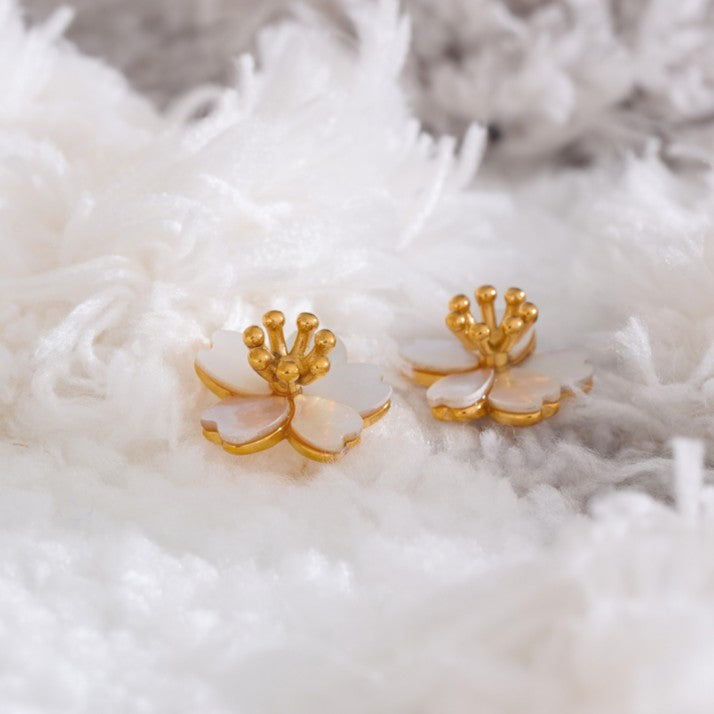 Gold and white floral earrings on a textured white surface
