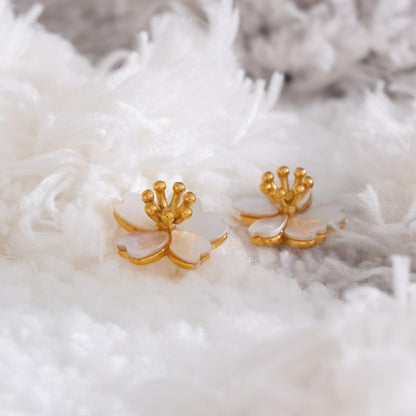 Gold and white floral earrings on a textured white surface