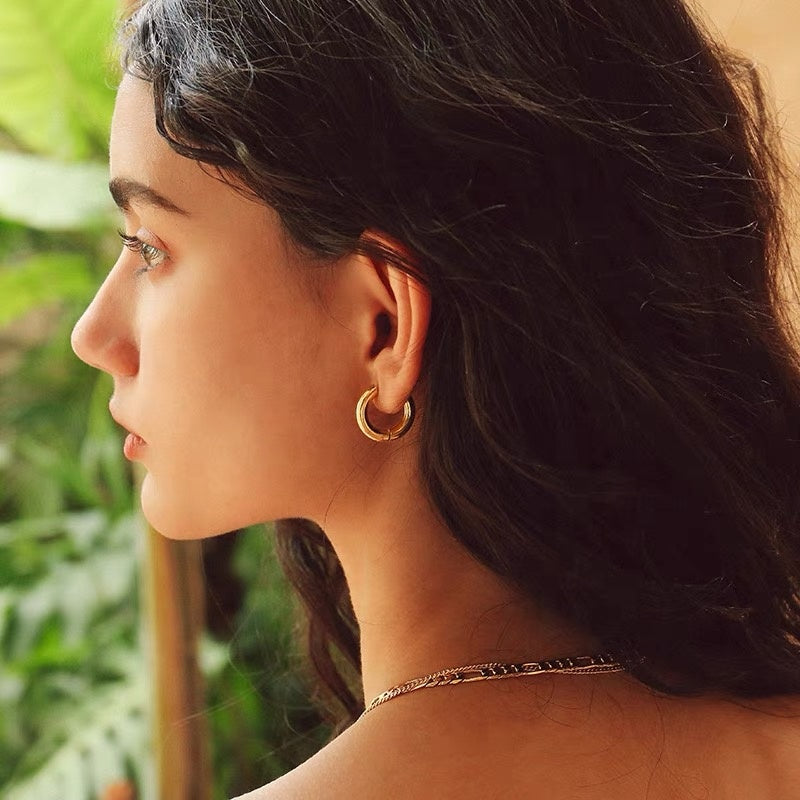 Close-up of a woman wearing gold hoop earrings with a blurred green background