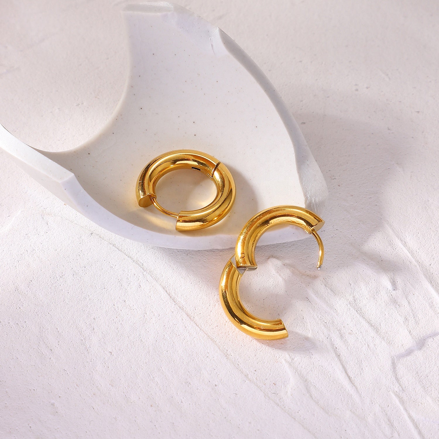 Minimalist gold hoop earrings on a white ceramic dish