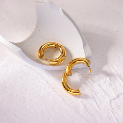 Minimalist gold hoop earrings on a white ceramic dish