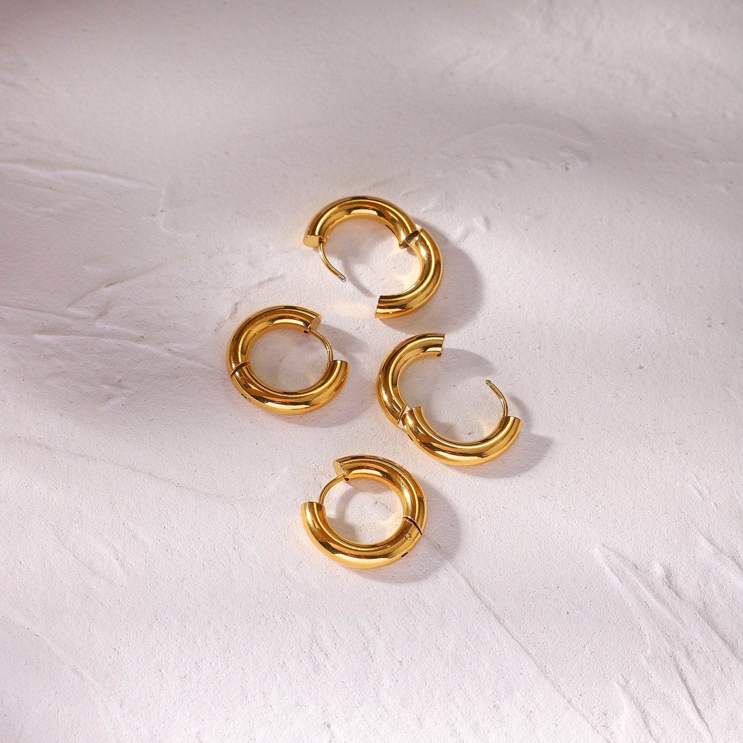 Gold waterproof hoop earrings on a textured white surface