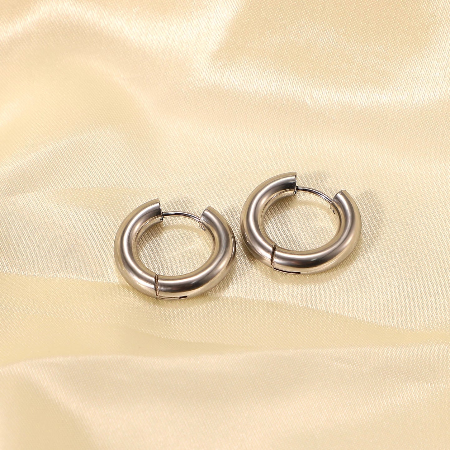 Pair of minimalist silver hoop earrings on a beige fabric background