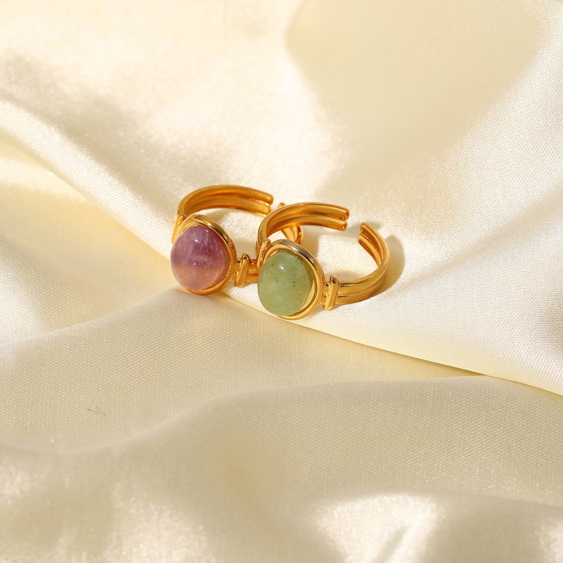 Gold ring with purple and green gemstones on a beige fabric background