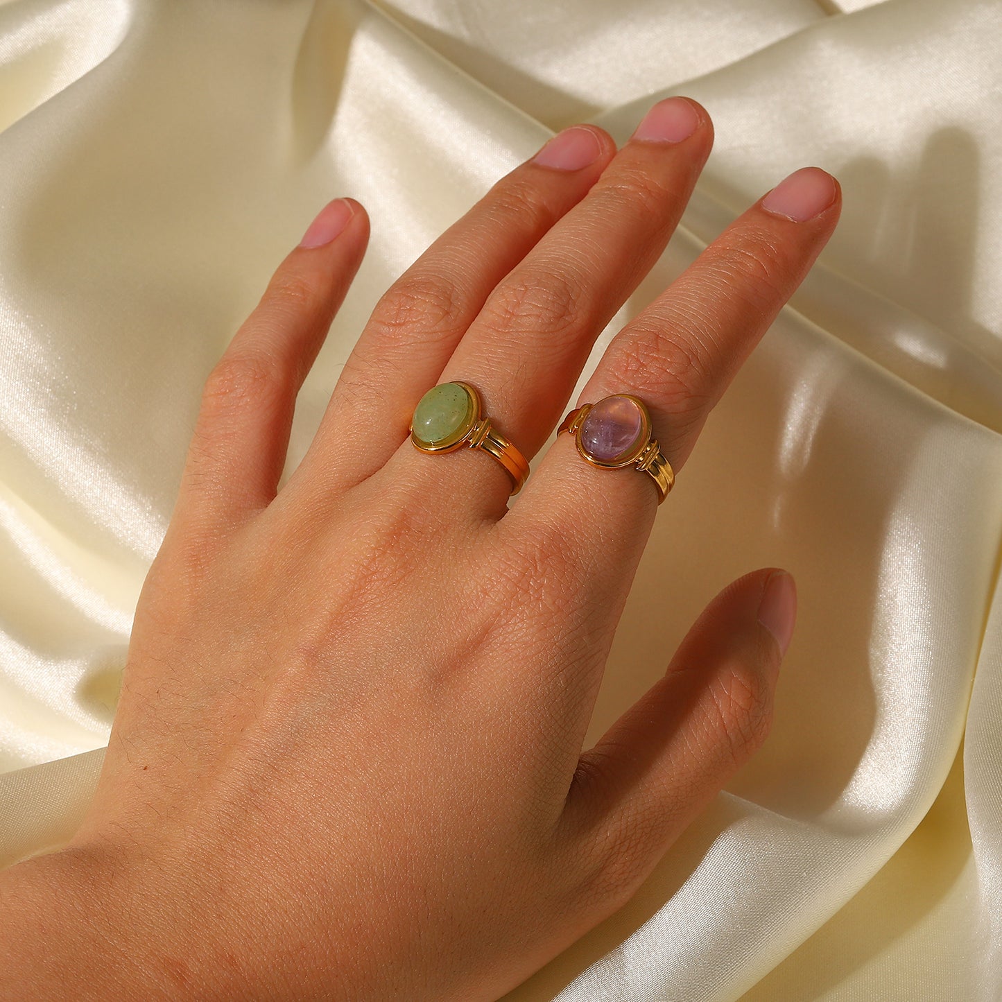 Hand wearing two gold rings with gemstones on a beige fabric background