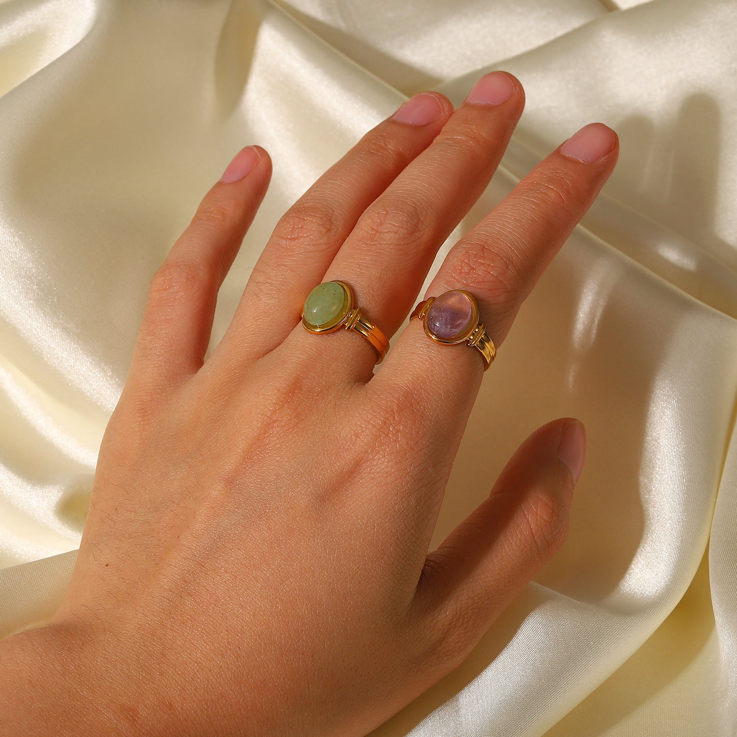 Hand wearing two gold rings with gemstones on a beige fabric background