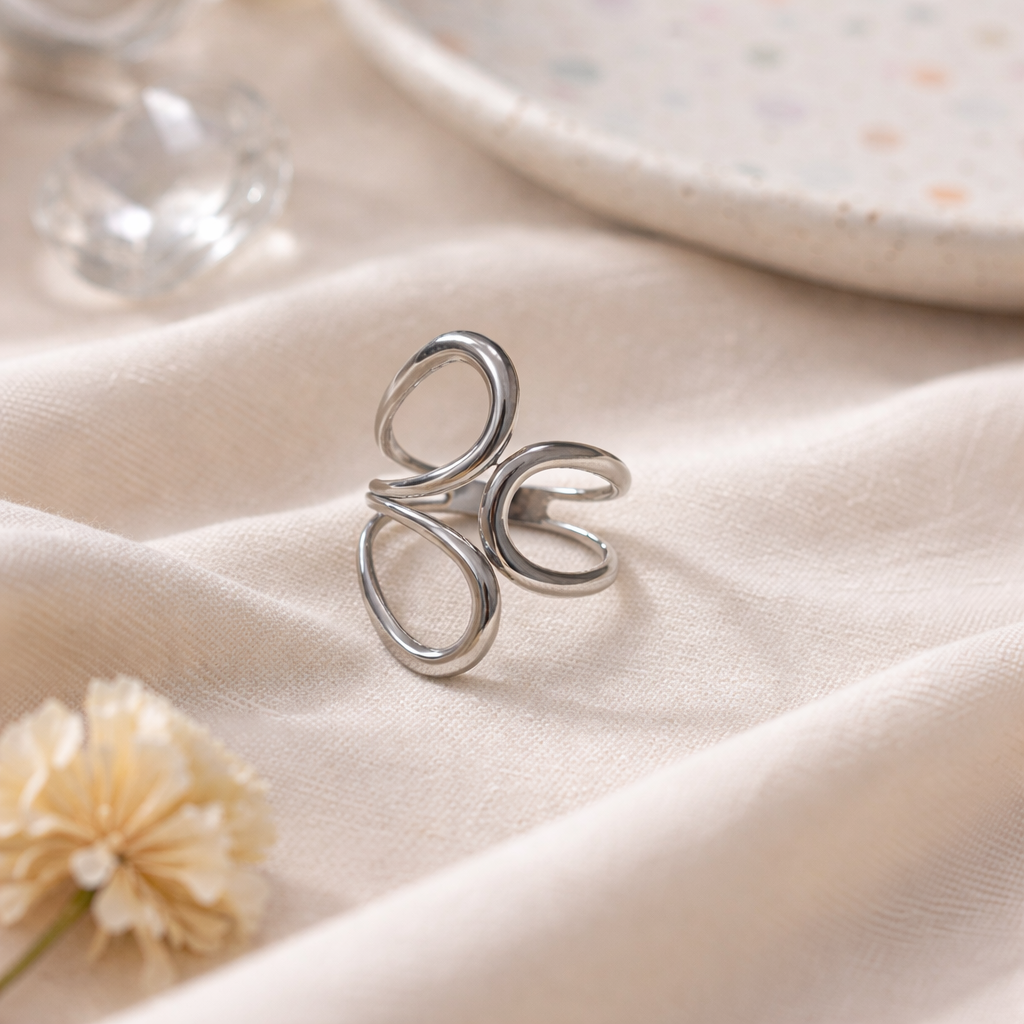 Silver ring on a soft fabric surface with a flower and glassware in the background