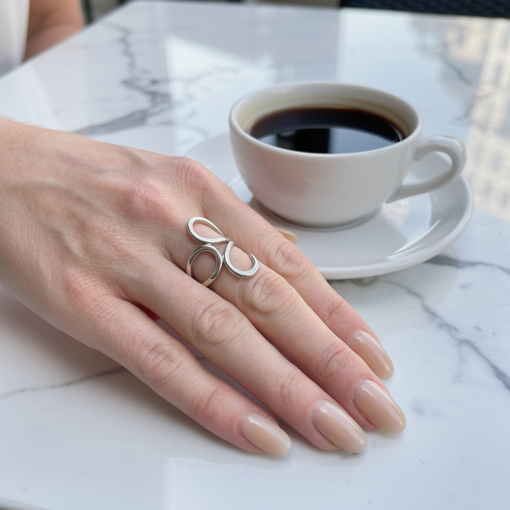 Hand wearing a silver waterproof ring with a cup of coffee on a marble surface