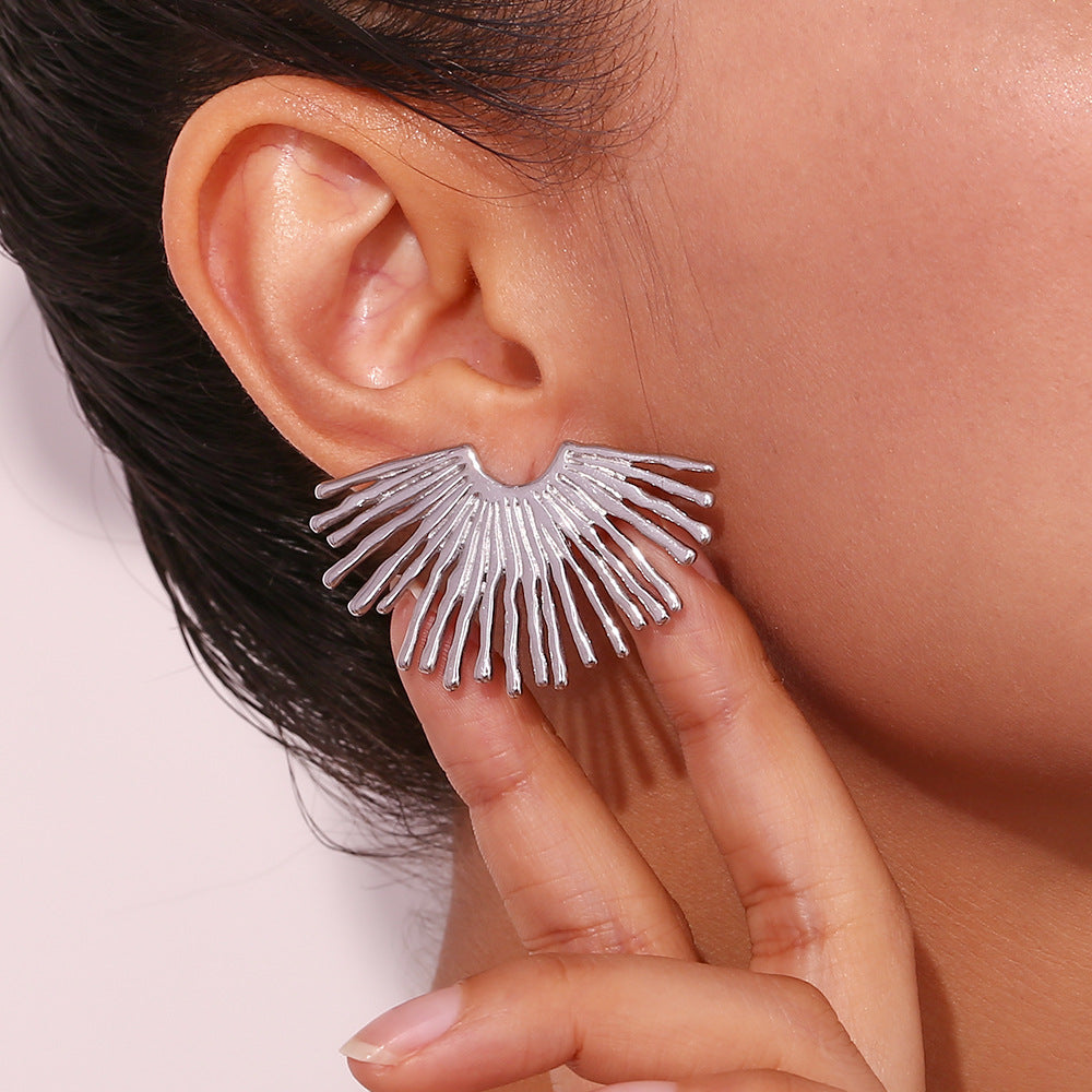 Silver fan-shaped earring worn by a person with a neutral background