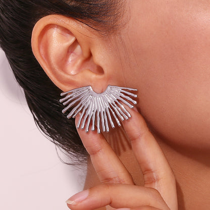 Silver fan-shaped earring worn by a person with a neutral background