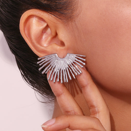 Silver fan-shaped earring worn by a person with a neutral background