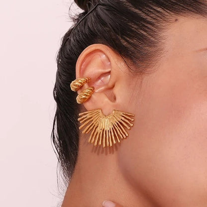 Gold statement earrings worn by a person with a plain background