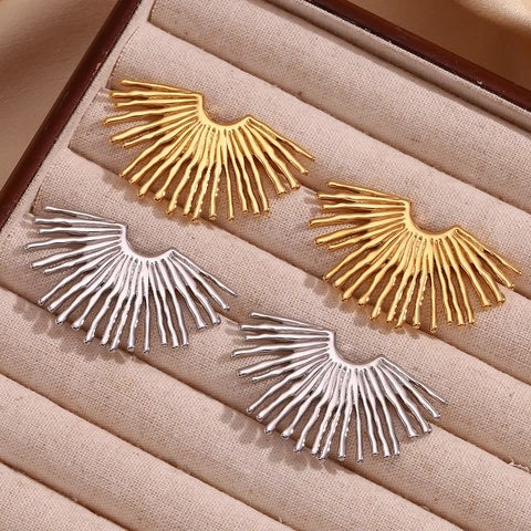 Pair of gold and silver waterproof earrings on a beige fabric surface
