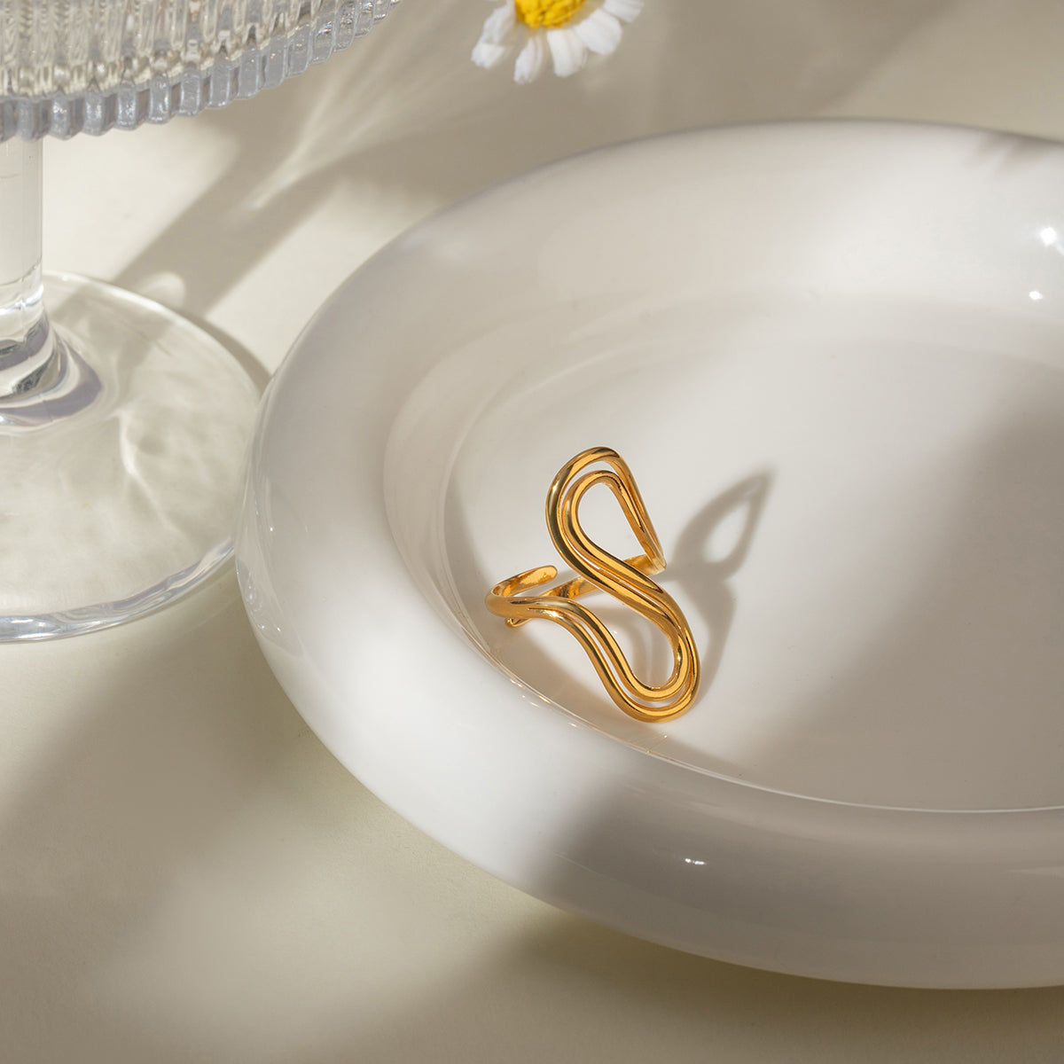 Gold ring on a white dish with a glass and flower in the background
