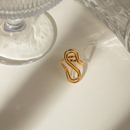 Gold ring with a unique design on a white surface with glassware in the background