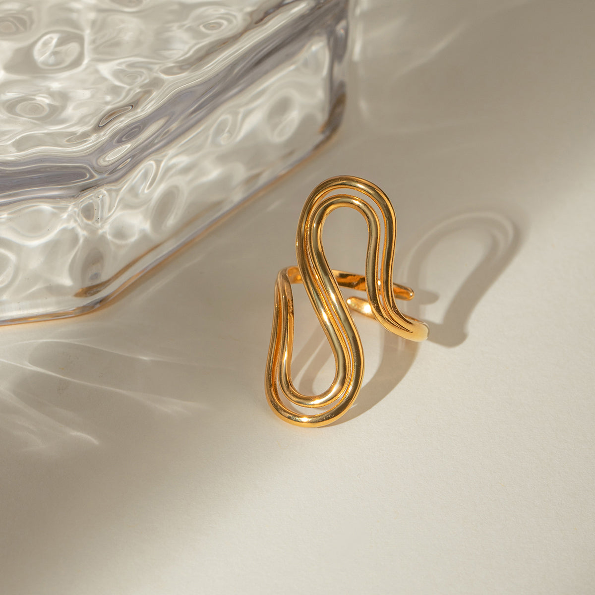 Gold spiral ring on a textured beige surface with a glass dish in the background
