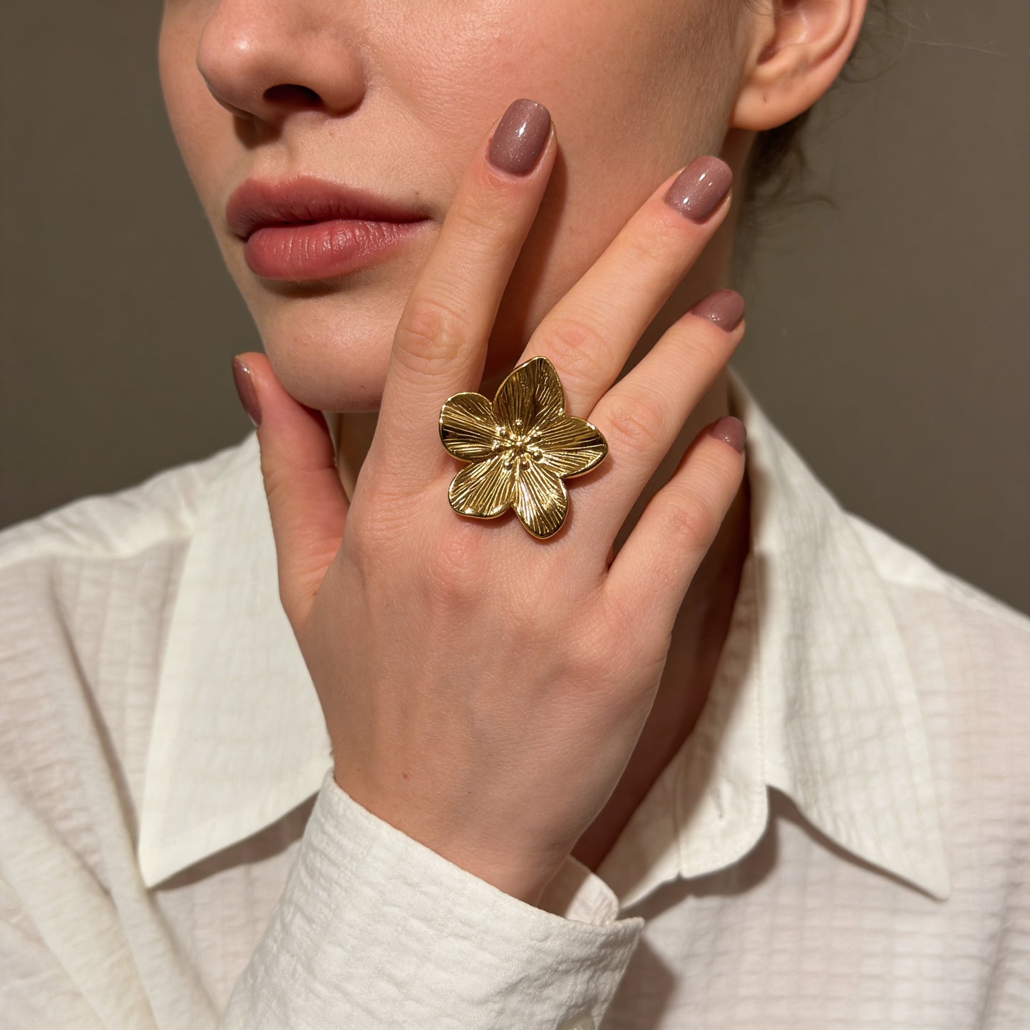 Close-up of a hand wearing a gold floral ring with a neutral background