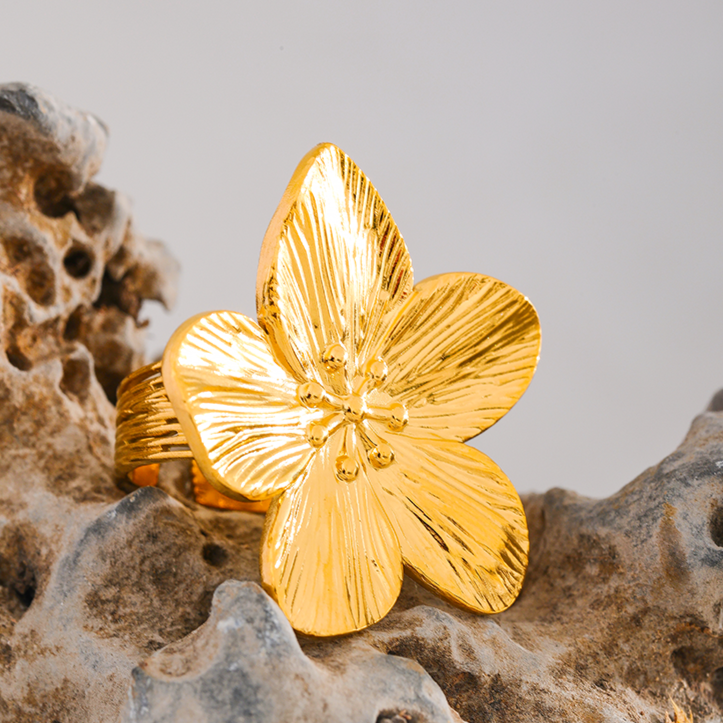 Gold flower-shaped ring on a textured surface with a neutral background