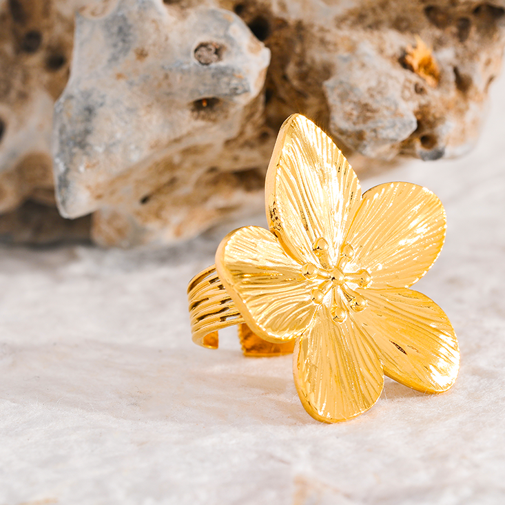 Gold flower-shaped ring on a textured surface with a natural background