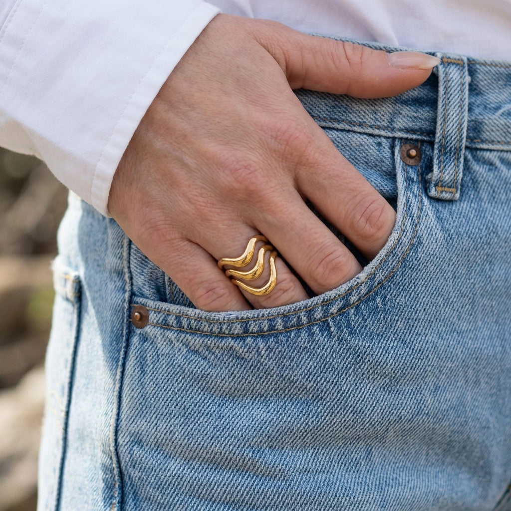 Hand wearing an elegant gold ring on a blue denim background